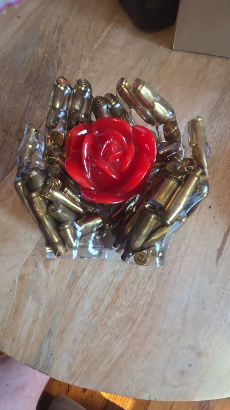 Cupped resin hands holding a red rose, filled with brass bullet shells